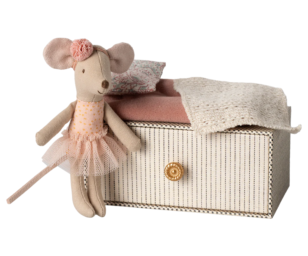 The Maileg Dancing Mouse in Daybed is dressed in a tutu and floral headband, appearing ready for a dance lesson, while standing beside a compact striped box featuring a round, gold-colored knob. The box is beautifully decorated with a pink cushion and a cream-colored knitted blanket.