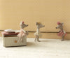 Three stuffed mice, dressed as ballerinas in pink, white, and peach tutus, partake in a ballet class. The Maileg Ballerina Mouse - Little Sister (Off White) joins them beside a small cushioned bench against a backdrop of a patterned beige wall. The ballerina mice seem absorbed in practicing their ballet poses and techniques.