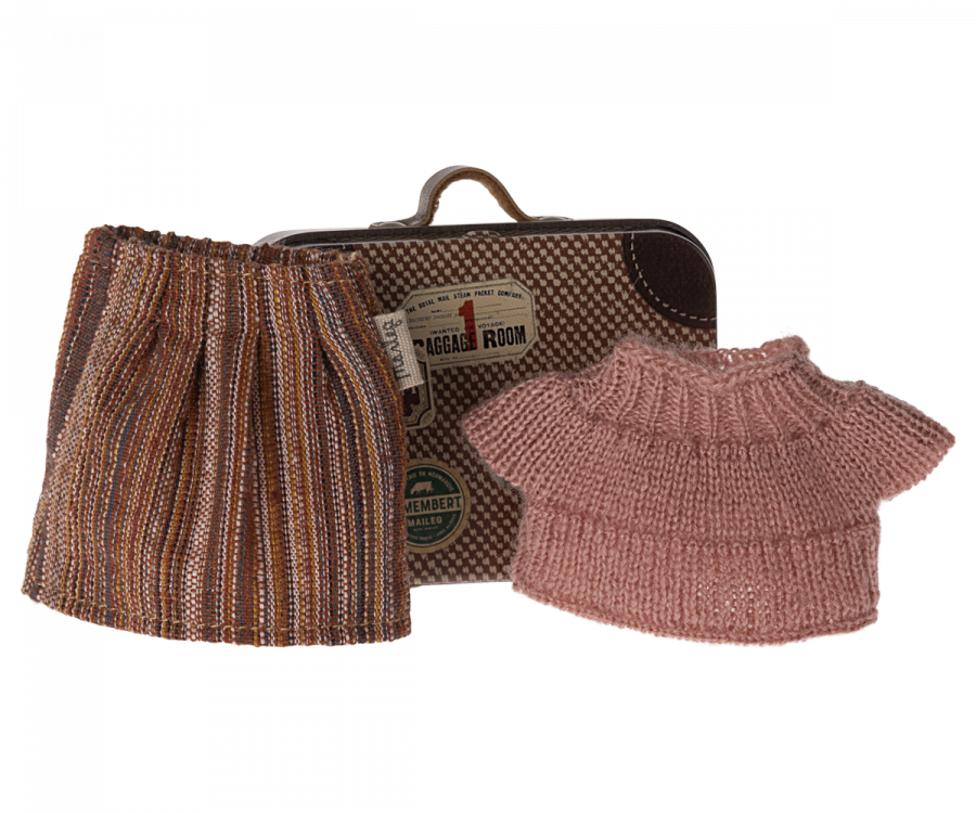 A small metal suitcase with travel stickers stands upright. In front of it are two pieces of Maileg Knitted Blouse And Skirt In Suitcase, Grandma Mouse: one is a multi-colored striped skirt, and the other is a pink short-sleeved sweater.