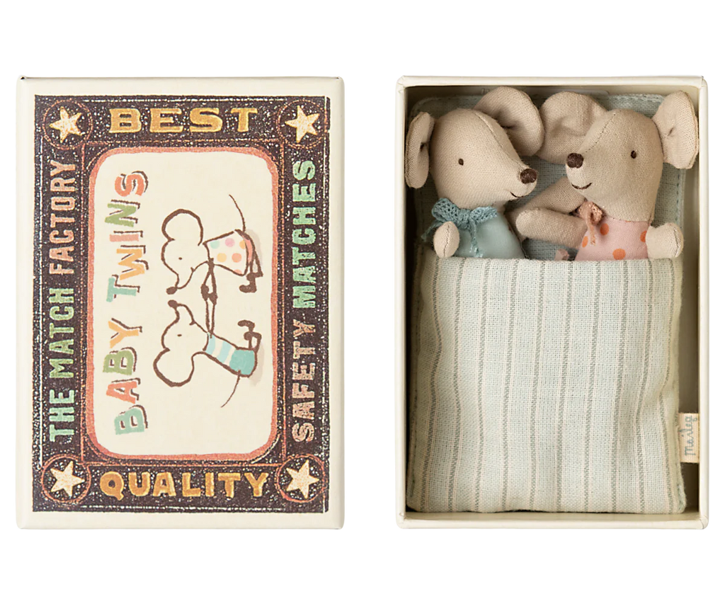 The product "PRE-ORDER: Maileg Twin Baby Mice In Matchbox" features vintage-style matchbox packaging decorated with baby mice illustrations. Inside the open box, two plush twin mice in pastel outfits nestle cozily in a striped fabric pocket, creating a charming matchbox bed. Ships late February.