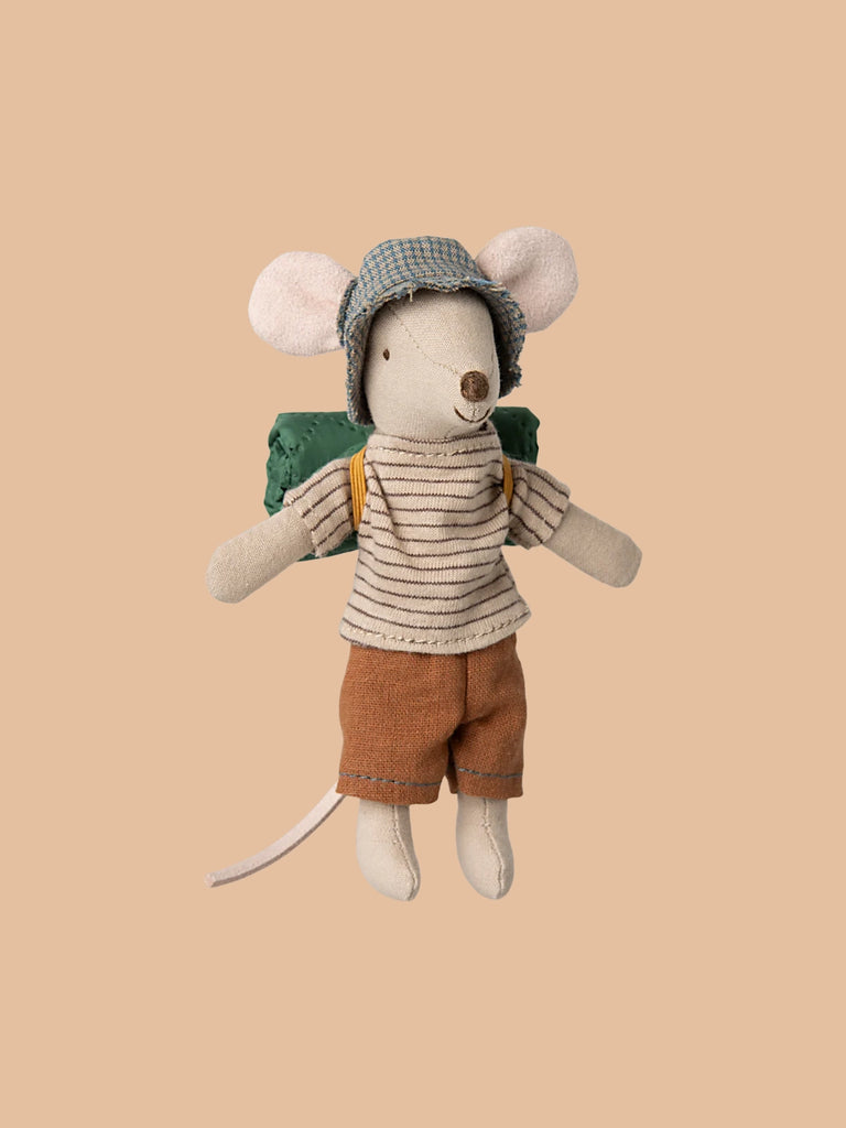 A Maileg Big Brother Horseback Adventure Set toy, dressed in a blue checked hat, striped shirt, brown shorts, and a green backpack, is posed against a plain beige background.