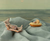 The Maileg Beach Mouse with Air Mattress - Dad lounges in plaid shorts on a blue air mattress, relaxing by an illustrated summer sea scene. Nearby, a yellow raft with a toy and cookie floats, tethered by string.