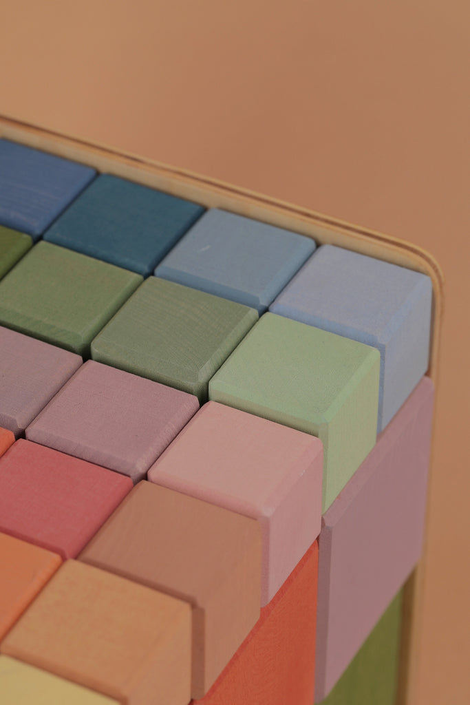Close-up of a stack of Raduga Grez Big Cube Block Set - Colorful neatly arranged in various shades of blue, green, and pink against a soft peach background.