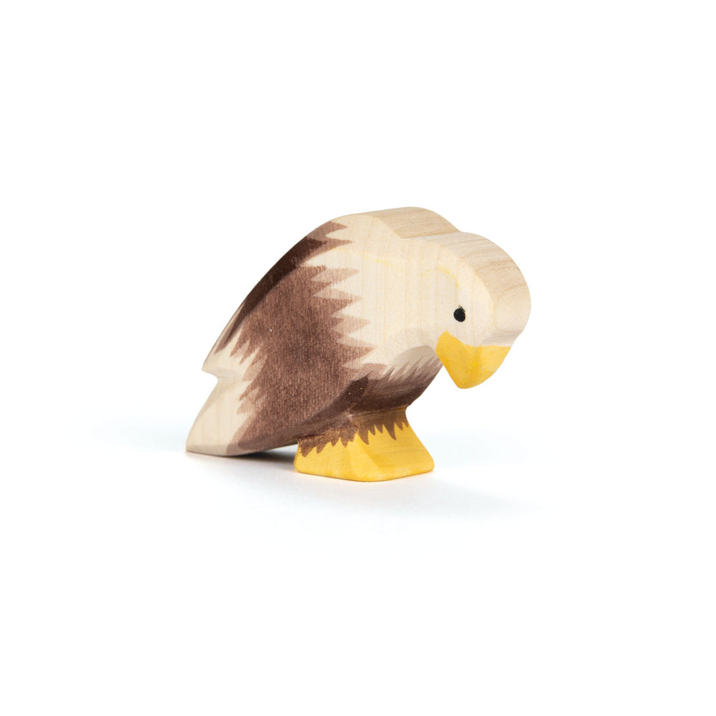 An Ostheimer Bird - Bald Eagle, Sitting: a handcrafted wooden figure with painted brown wings, white head, and yellow beak and feet, displayed on a white surface.