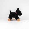 Pull-Along Walter is a black plush dog with a red collar, mounted on a wooden wheeled base and featuring a white pull string. This engaging pull-along toy encourages the development of gross motor skills and is presented against a plain white background.