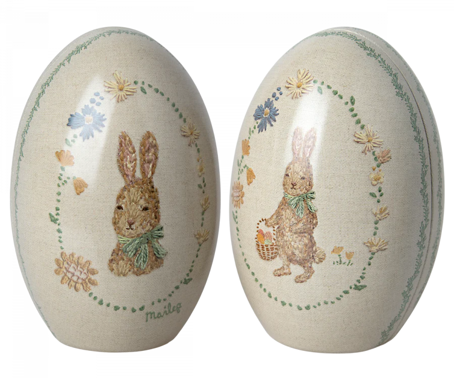 The Maileg Easter Egg set includes two metal eggs with vintage-style Dorthe Mailil illustrations. One features a rabbit in a scarf amid flowers, the other with a basket, on textured beige backgrounds. These charming pieces ship in approximately one week and make perfect decorations!.