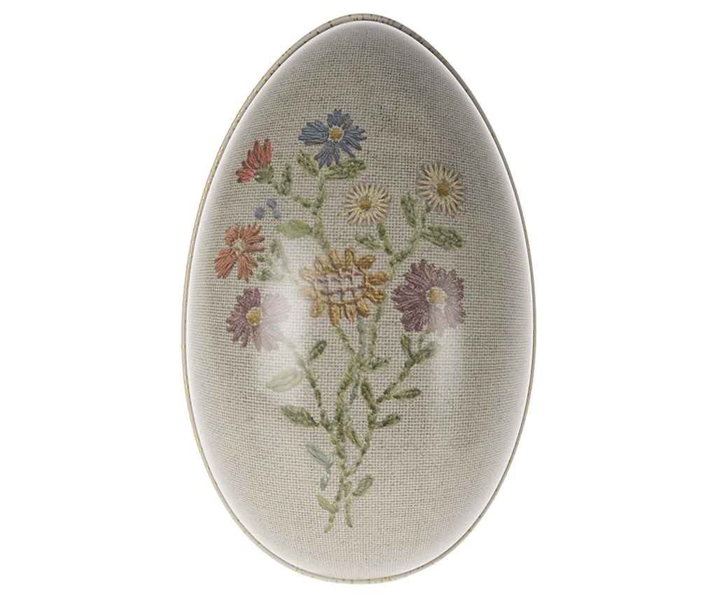 An oval-shaped Maileg Easter Egg, decorated with detailed, colorful flowers and leaves designed by Dorthe Mailil, set against a soft grey striped background.