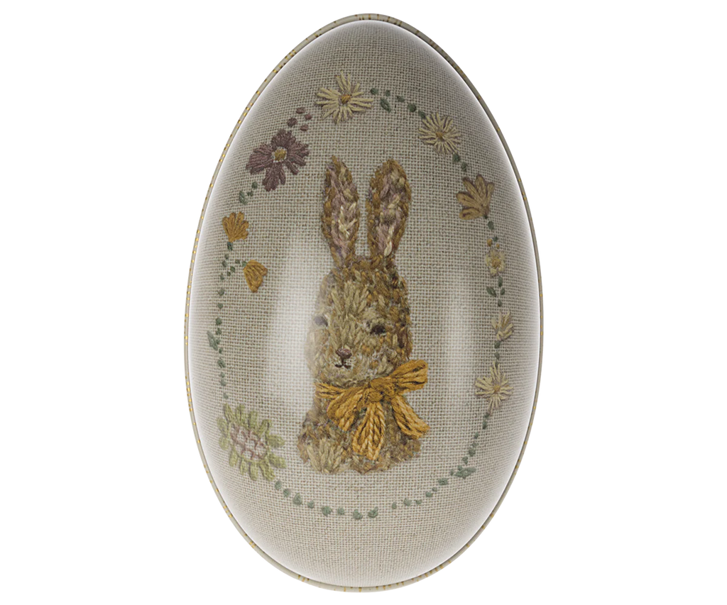 An oval-shaped Maileg Easter Egg featuring a detailed depiction of a brown bunny with a bow around its neck, surrounded by floral accents, set against a beige background.
