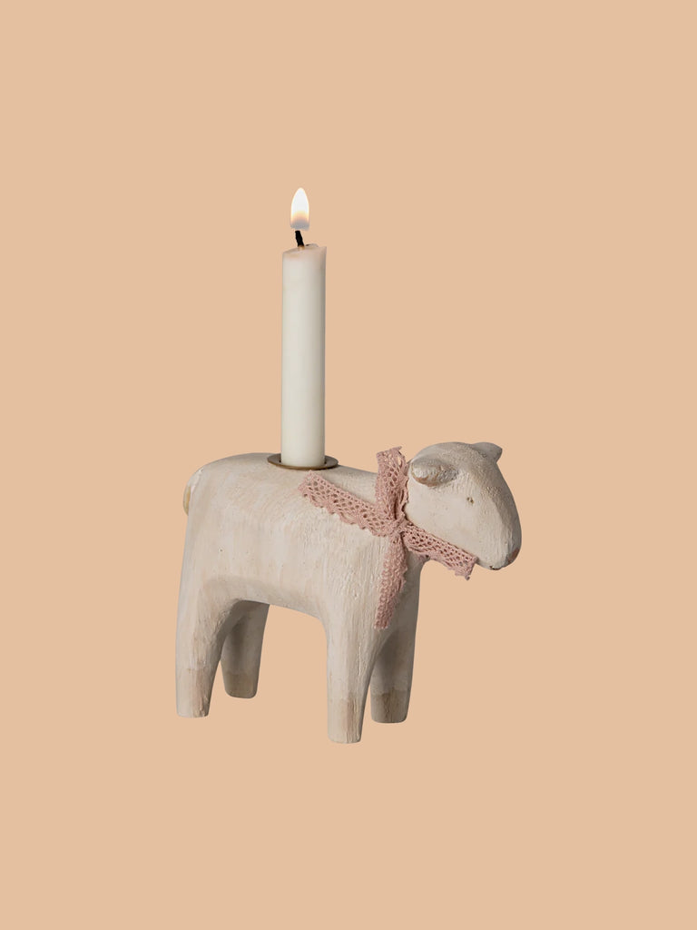 The PRE-ORDER Maileg Wooden Candle Holder - Rose Lamb, shipping late January, is a charming handmade figurine with a pink ribbon and serves as an Easter centerpiece. A lit white candle sits gracefully on its back against a simple beige background.