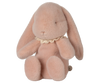 The pre-order Maileg Easter Egg With Bunny in powder pink features a soft plush bunny made from recycled polyester, with long ears, closed eyes, and a lace collar. It sits upright, highlighting its fluffy texture and contains PE pellets for stability. Ships in February.