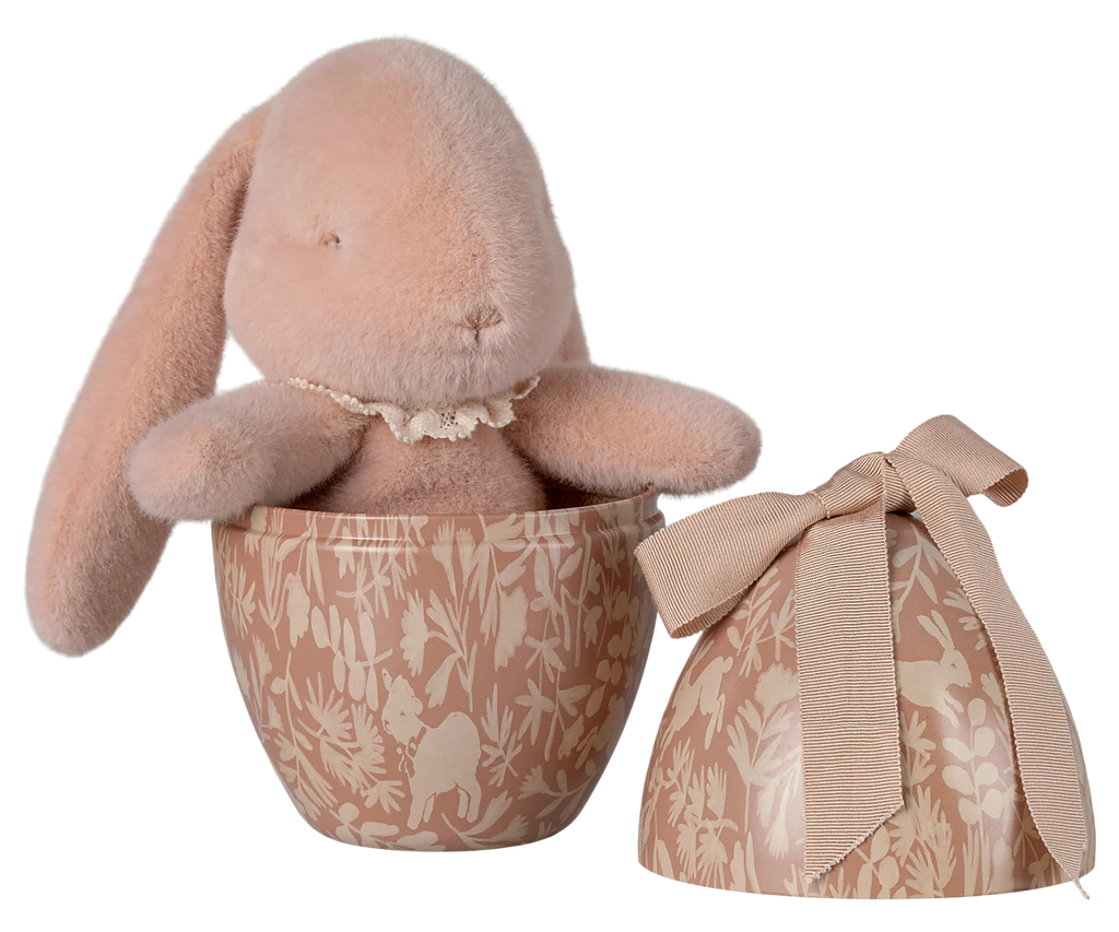 A pink plush bunny is nestled inside the Maileg Easter Egg With Bunny - Powder, a beige, patterned egg-shaped container made from recycled polyester with floral and rabbit designs. The matching lid features a beige bow. Ships in February.