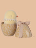 Nestled in a floral-patterned egg-shaped container of recycled polyester, a plush yellow chick with a lace collar and the matching lid tied with a pink ribbon awaits on a light peach surface. Introducing the PRE-ORDER: Maileg Easter Egg With Chick (Ships in February).