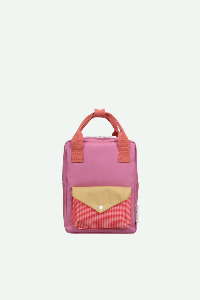 The Sticky Lemon Backpack Small - Envelope - Rosebay Pink is a compact pink backpack with orange handles and a front pocket adorned with a yellow flap and red checkered fabric, set against a plain white background. Made from recycled PET bag materials and featuring adjustable shoulder straps, it’s perfect for little ones on the go. Ships in a week.