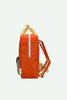 The Sticky Lemon Backpack Medium | Envelope | Campfire Orange is shown from the side, featuring a campfire orange color with beige straps and a white zipper running vertically on the front. Crafted from recycled PET bottles and finished with a waterproof lining, this backpack offers both sustainability and style. The background is plain and light-colored.