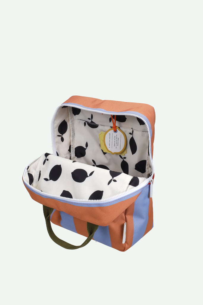 A medium-sized Sticky Lemon Backpack in Stripes (Cloud Blue + Maple Whirl) features brown and light blue stripes, unzipped to reveal a white interior with a black pear pattern and waterproof lining. The bag has olive green handles and a yellow tag attached inside.