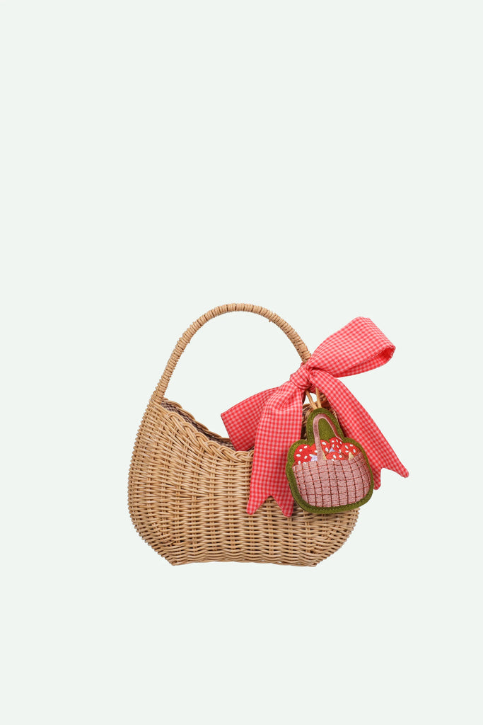 A charming Sticky Lemon Wicker Basket | Lemon Tree featuring a curved handle, adorned with a large red gingham bow and a small embroidered strawberry bag charm hanging from the handle—a delightful kids accessory for any outing.