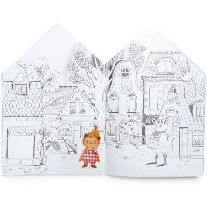 The Moulin Roty Coloring Book with Stickers – The Minouchkas features a black-and-white street scene with houses, trees, two adults walking, and a colorful Minouchkas doll in a red checked dress standing out in the foreground.