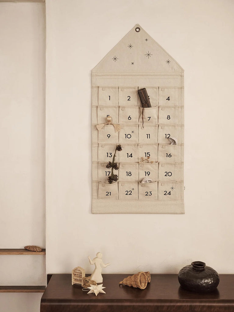 Ferm Living Star Christmas Calendar - Sand/Black wall-mounted canvas house advent calendar with twenty-four numbered pockets, each featuring assorted small Christmas decorations.