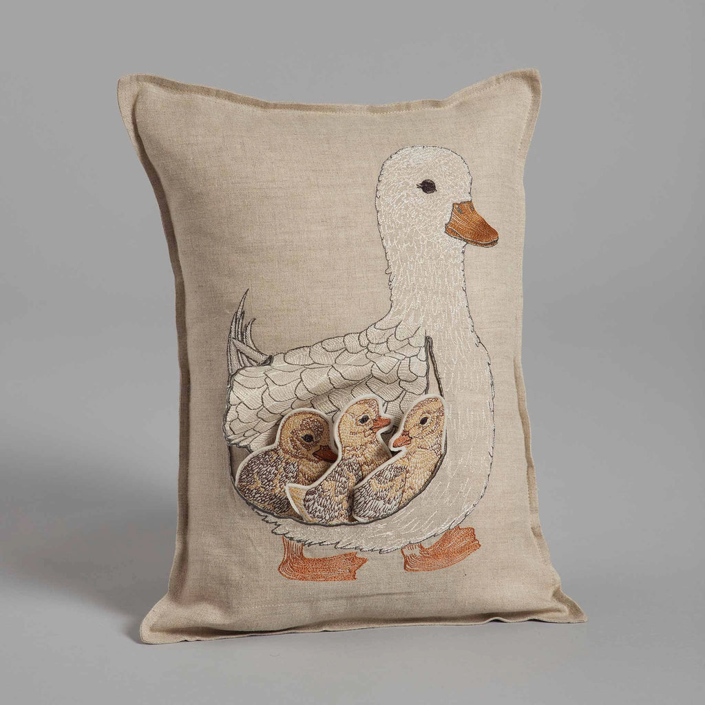 Decorative pillow featuring an embroidered design of a Coral & Tusk Mama Duck Pocket Pillow with three removable ducklings on a neutral linen background.