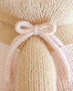 Close-up of a light pink knitted bow tied around the back of Cuddle + Kind Kelsie the Pony, a beige, hand-knit doll. Detailed yarn textures highlight this charming creation, handmade in Peru.