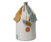 The Maileg Basket, made from cotton linen and designed in the shape of a circus tent, showcases a multicolored scalloped top adorned with pom-pom accents and features a convenient drawstring closure. Ideal for toy storage, it has a white base decorated with large colored circles.