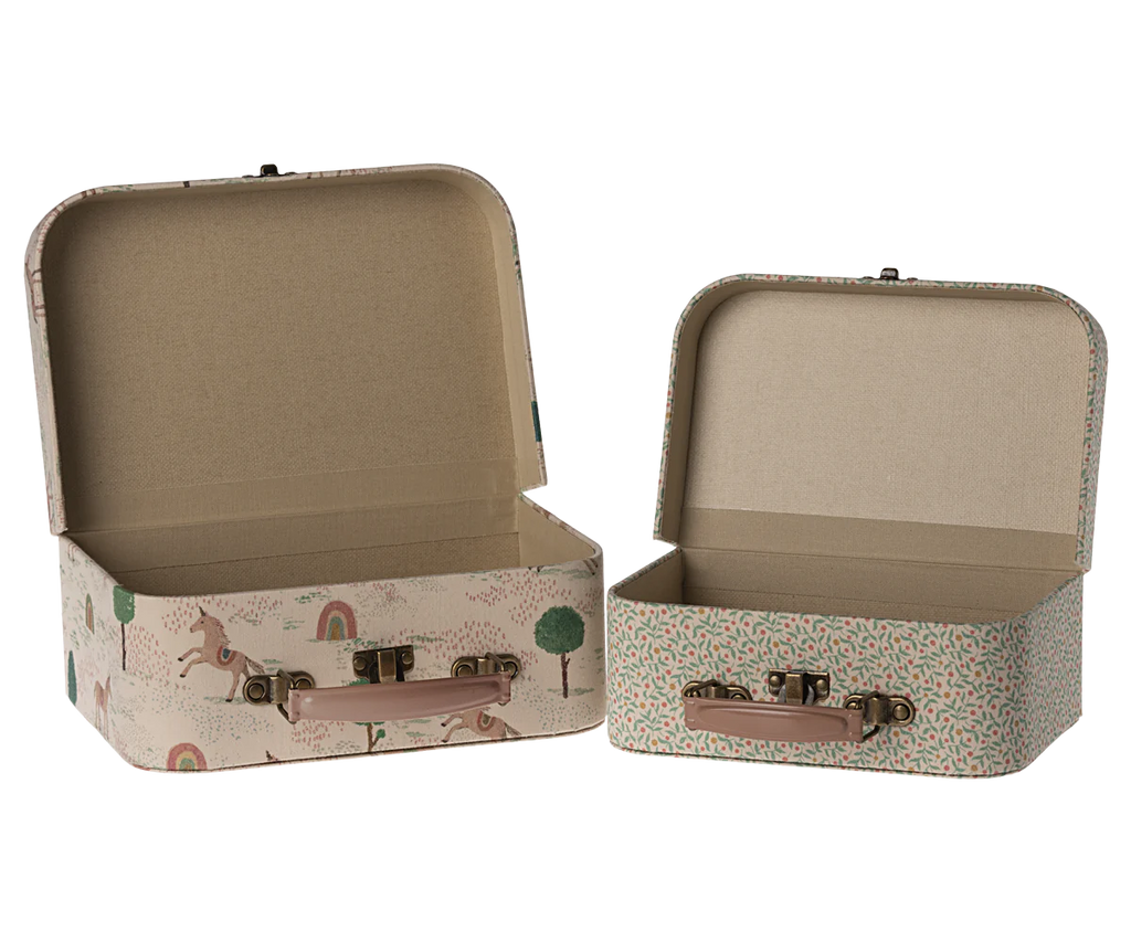 Two small, open suitcases with whimsical designs are part of the Maileg 2 Piece Suitcase Set. The larger suitcase on the left showcases delightful drawings of animals, trees, and rainbows against a light beige background. Meanwhile, the smaller suitcase on the right boasts a lush green leaf pattern set on a pink background. Both suitcases have brown handles and are perfect for adding charm to your storage solutions.