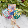A Pollinator Seed Pop (Single) labeled "Plant Me!" is shown on snow by evergreen branches—perfect for starting a vibrant wildflower pollinator garden.