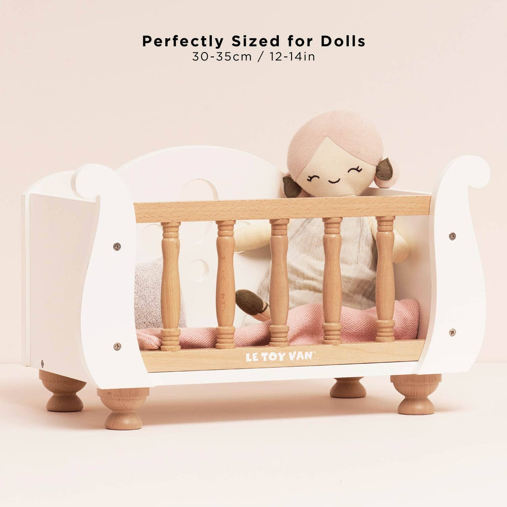 Wooden Dolls Cot featuring white wood with light wood railings and legs, containing a cloth doll and soft bedding, with text stating it is perfectly sized for 30-35cm / 12-14in dolls.