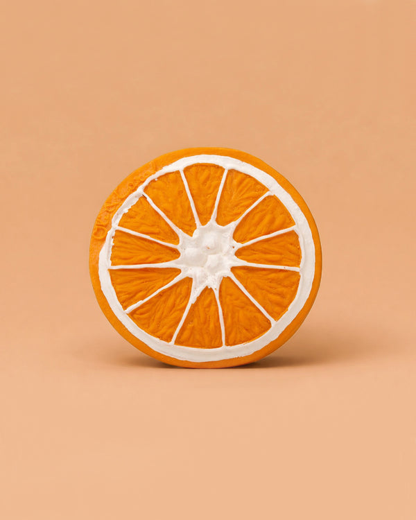 Clementino the Orange Teether is a round, orange natural rubber toy with white segment lines, resting on a peach background. Its textured surface is perfect for sensory play and soothing teething.
