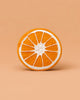 Clementino the Orange Teether is a round, orange natural rubber toy with white segment lines, resting on a peach background. Its textured surface is perfect for sensory play and soothing teething.
