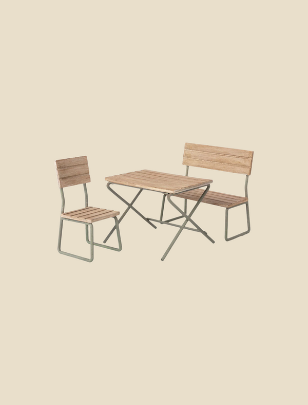 A vintage garden set of outdoor patio furniture featuring a wooden slatted chair, a wooden slatted bench with a backrest, and a rectangular wooden slatted table. Made with FSC certified, responsibly sourced wood, the minimalist design boasts metal frames and a light, natural wood finish. This is the Maileg | Miniature Garden Table Set.