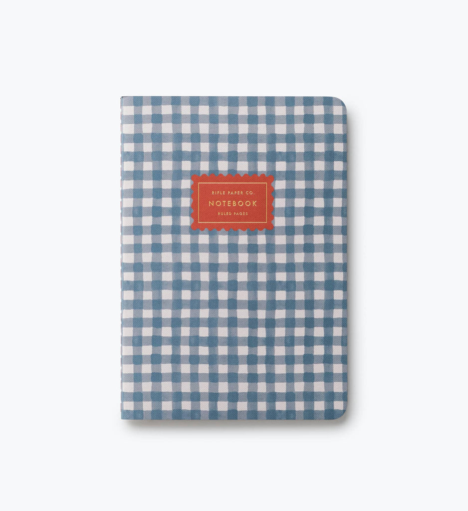 An Assorted Set of 3 Schoolhouse Notebooks, each featuring a blue and white checkered cover with a red “NOTEBOOK” label centered on the front, lay-flat binding for easy writing, displayed against a plain light gray background.