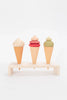 Three Handmade Ice Cream Cones with different colored scoops, painted with non-toxic water-based paint, displayed on a small wooden rack against a plain white background.