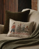 A beige couch features a dark green pillow, green knitted throw, and Coral & Tusk Christmas Tree Sled Pillow with embroidered animals in winter clothes riding a sled, placed in front of the larger pillow.