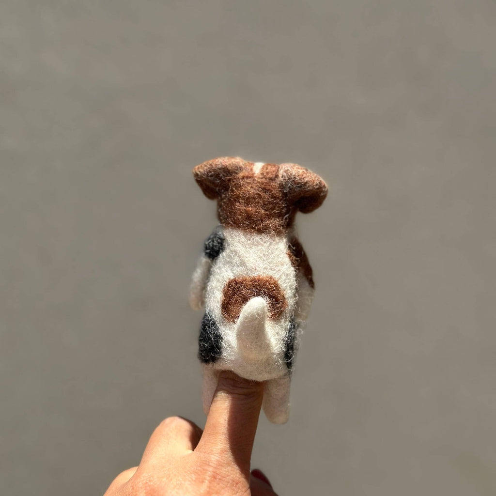 A hand holds the Felt Finger Puppet: Jack Russell Terrier Dog, featuring brown, black, and white spots, as seen from the back against a plain light background.
