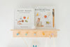 Two “Wishy Washy (Water Reveal Edition)” children's books sit on a light wooden shelf with pastel pegs. The right book features a reusable water-reveal activity and brush, perfect as a toddler travel activity or early learning gift.
