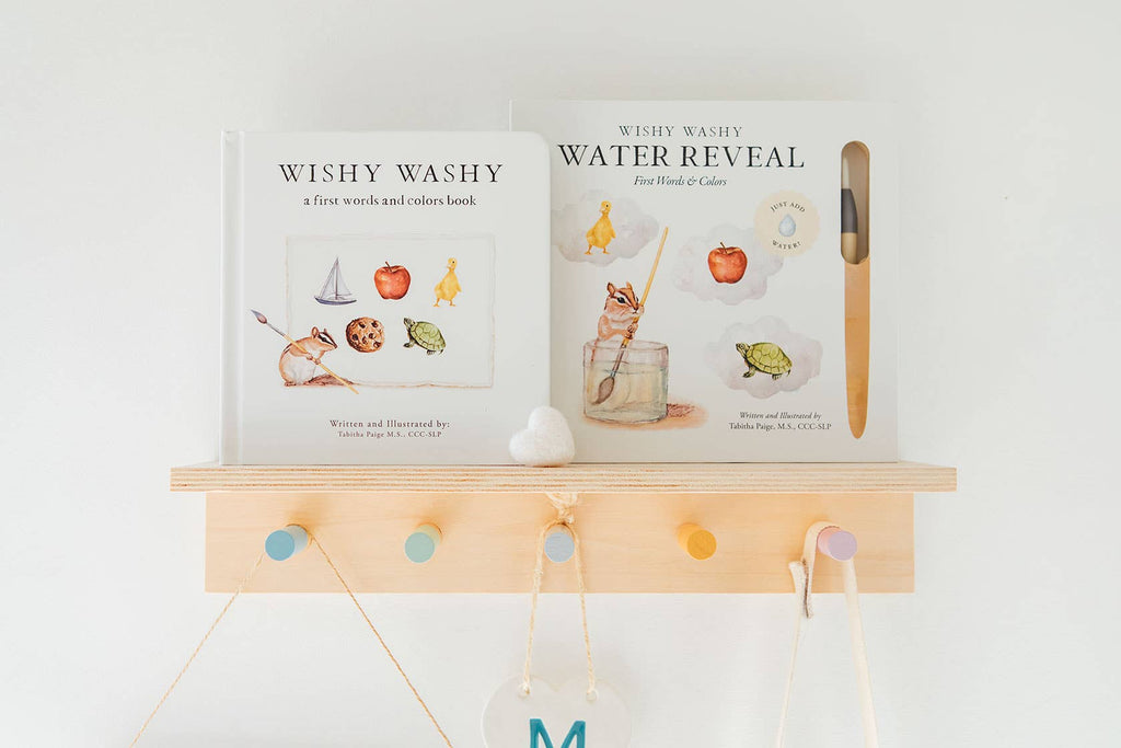 Two “Wishy Washy (Water Reveal Edition)” children's books sit on a light wooden shelf with pastel pegs. The right book features a reusable water-reveal activity and brush, perfect as a toddler travel activity or early learning gift.