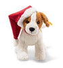 The Steiff Snuffy Puppy Dog Plush features brown and white fur with a red Santa hat playfully tilted to one side. It has black eyes and a stitched nose, creating a festive appearance.