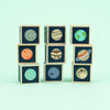 A stack of Uncle Goose Planet Blocks, each with illustrations of different solar system planets on a cool-toned background, displayed against a light aqua backdrop.