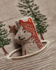 The Coral & Tusk Winter Foxes Pocket Pillow features an embroidered fox peeking from a pocket, with detailed trees and a small deer in the background—an ideal winter fox décor or animal nursery accent on soft beige fabric.