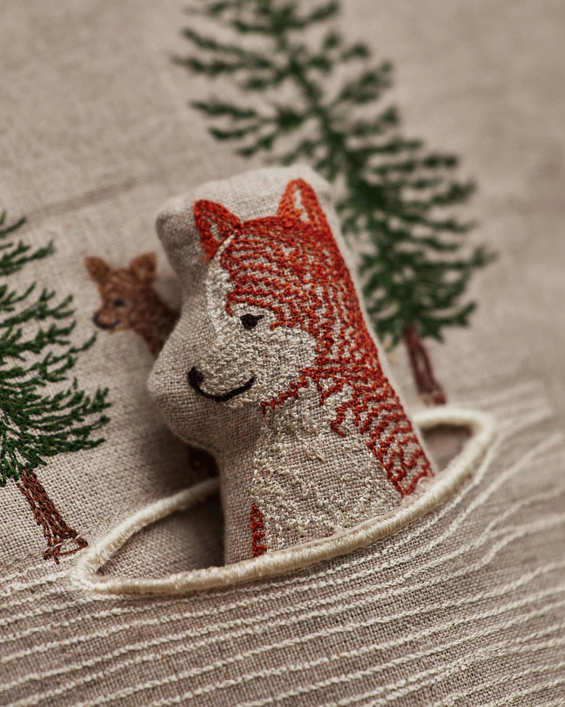 The Coral & Tusk Winter Foxes Pocket Pillow features an embroidered fox peeking from a pocket, with detailed trees and a small deer in the background—an ideal winter fox décor or animal nursery accent on soft beige fabric.