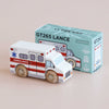 A wooden toy ambulance from No. 43 GT265 Lance | Made in England, featuring red stripes, is displayed beside its light blue box adorned with an illustration of the ambulance and the “GT265 LANCE” text. Perfect for imaginative play, this charming toy encourages children to invent their own rescue adventures.