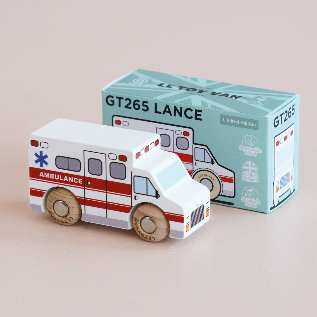 A wooden toy ambulance from No. 43 GT265 Lance | Made in England, featuring red stripes, is displayed beside its light blue box adorned with an illustration of the ambulance and the “GT265 LANCE” text. Perfect for imaginative play, this charming toy encourages children to invent their own rescue adventures.