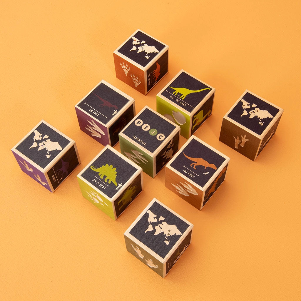 Several Uncle Goose Dinosaur Blocks arranged on an orange background, suggesting a themed board game or educational activity.