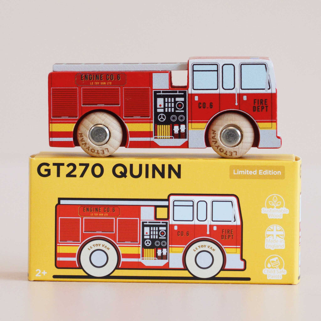 A wooden fire engine labeled “Engine Co. 6” sits atop a yellow box marked “No. 44 GT270 Quinn | Made in England,” featuring illustrations that match the toy inside. Designed for ages 2 and up, this charming toy is perfect for imaginative adventures and heroic rescue missions.