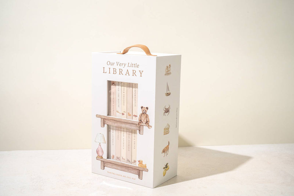 The "Our Very Little Library Board Book Set" showcases adorable animal and object illustrations. The box, designed with a handle, organizes the books like a mini bookshelf, ideal for introducing first words and growing your baby's vocabulary.