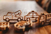 The Service Vehicle Cutter Set - Eco Playdough Tool is displayed on a wooden surface in warm natural light alongside wooden toy vehicles—a tow truck, police car, and fire truck—perfect for inspiring sensory play or pairing with transport-themed accessories.