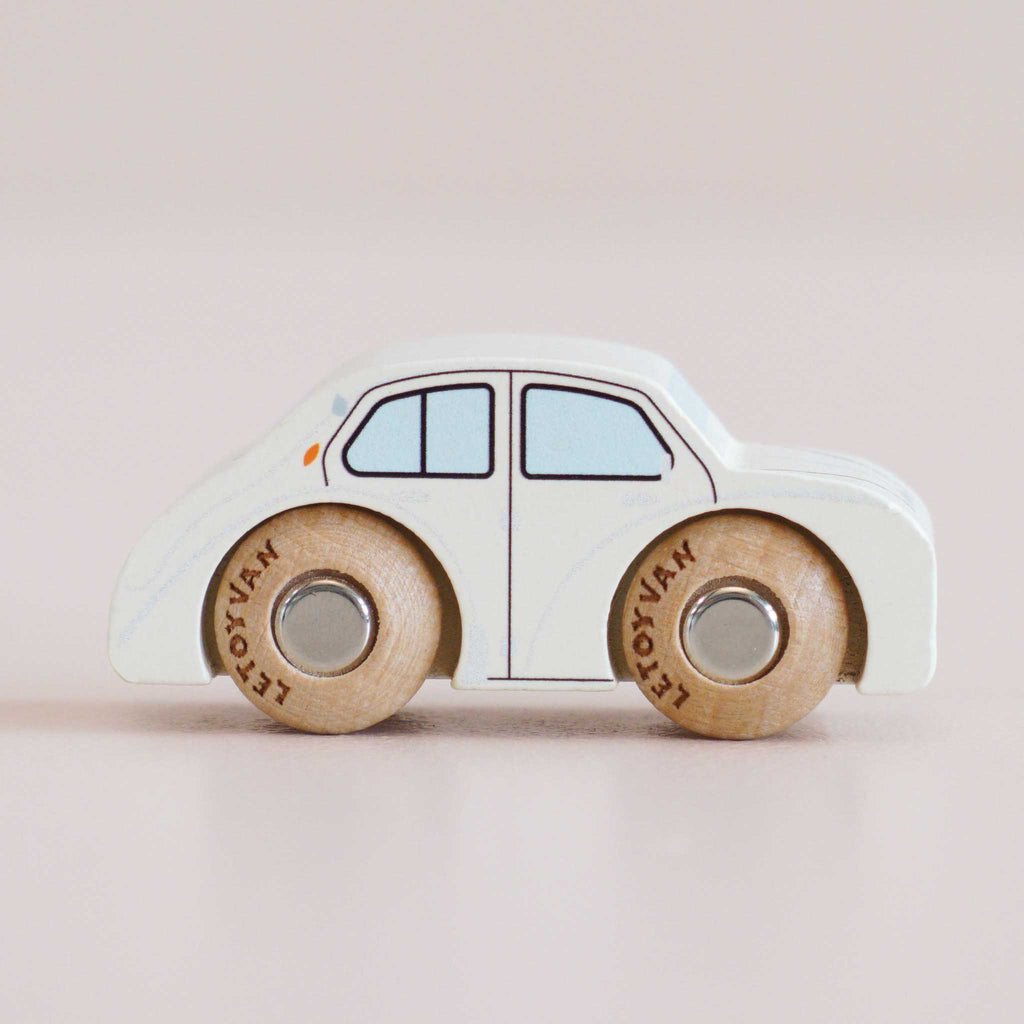 Introducing the No. 20 GT110 Rene, handcrafted in England—a small white wooden car featuring minimal blue windows, tan wooden wheels, and sturdy metal axles. Displayed on a soft pink background, it’s perfect for imaginative play and brings timeless charm to any classic toy collection.