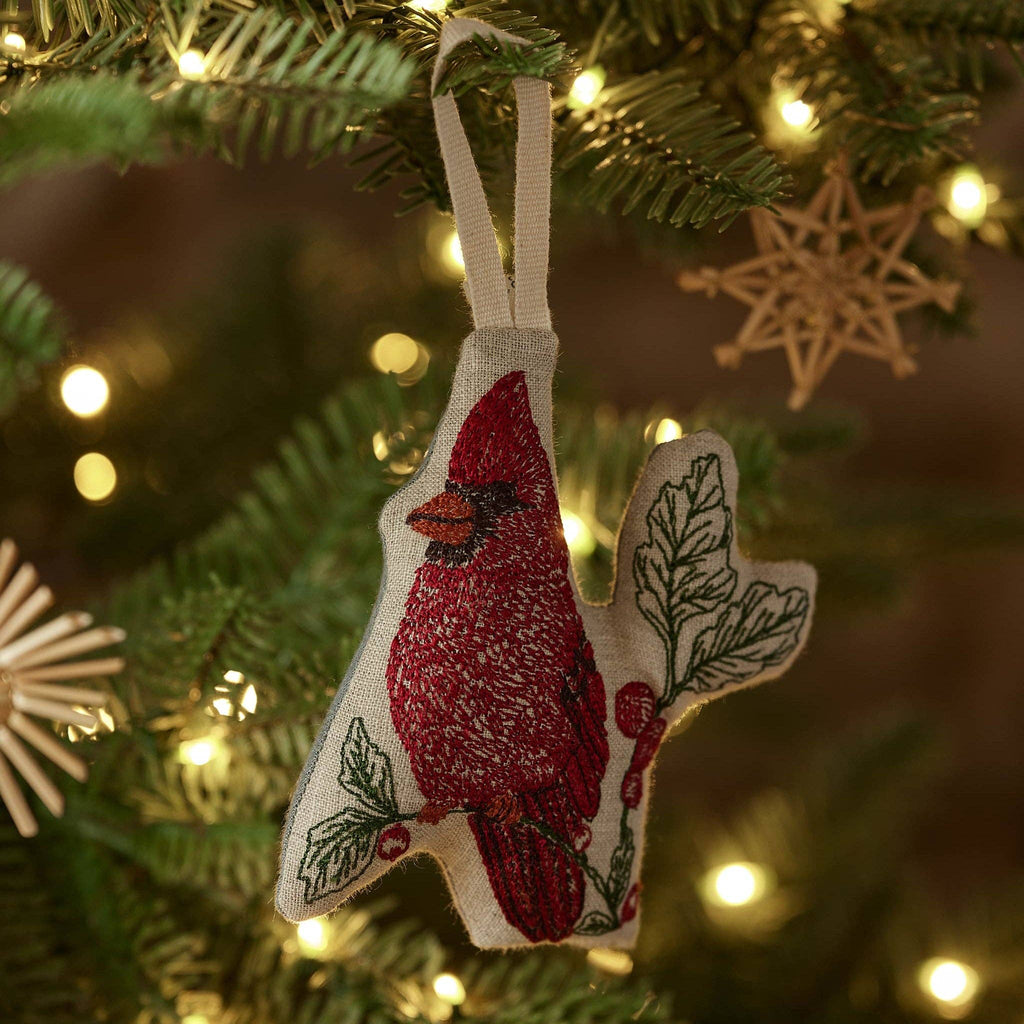 A Coral & Tusk Red Cardinal Ornament embroidered on natural linen, hanging from a Christmas tree.