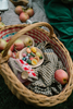 The Grapat Play Set - Fruits, wooden apples, a checkered cloth, and a knitted pouch sit in a wicker picnic basket on an outdoor blanket, inviting open-ended play.